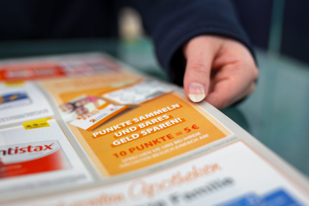 Hand, die ein Werbeangebot zum Punkte sammeln und Geld sparen auf einem Flyer hält. In der Trommsdorff Apotheke in Erfurt