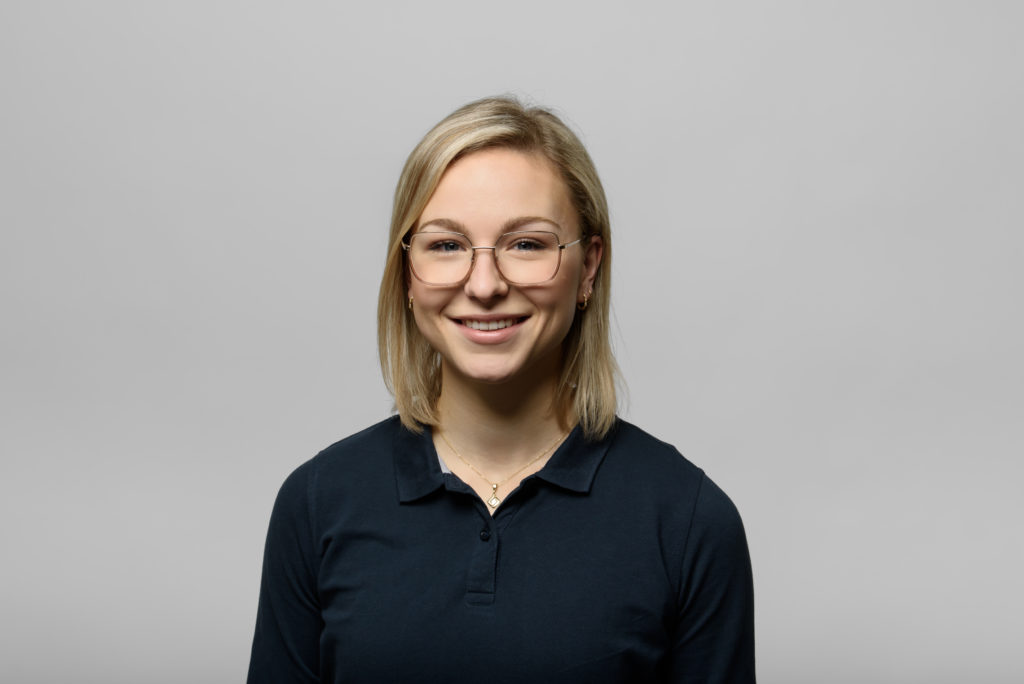 Eine lächelnde Person mit kurzen blonden Haaren und Brille, die ein schwarzes Poloshirt trägt. In der Trommsdorff Apotheke in Erfurt