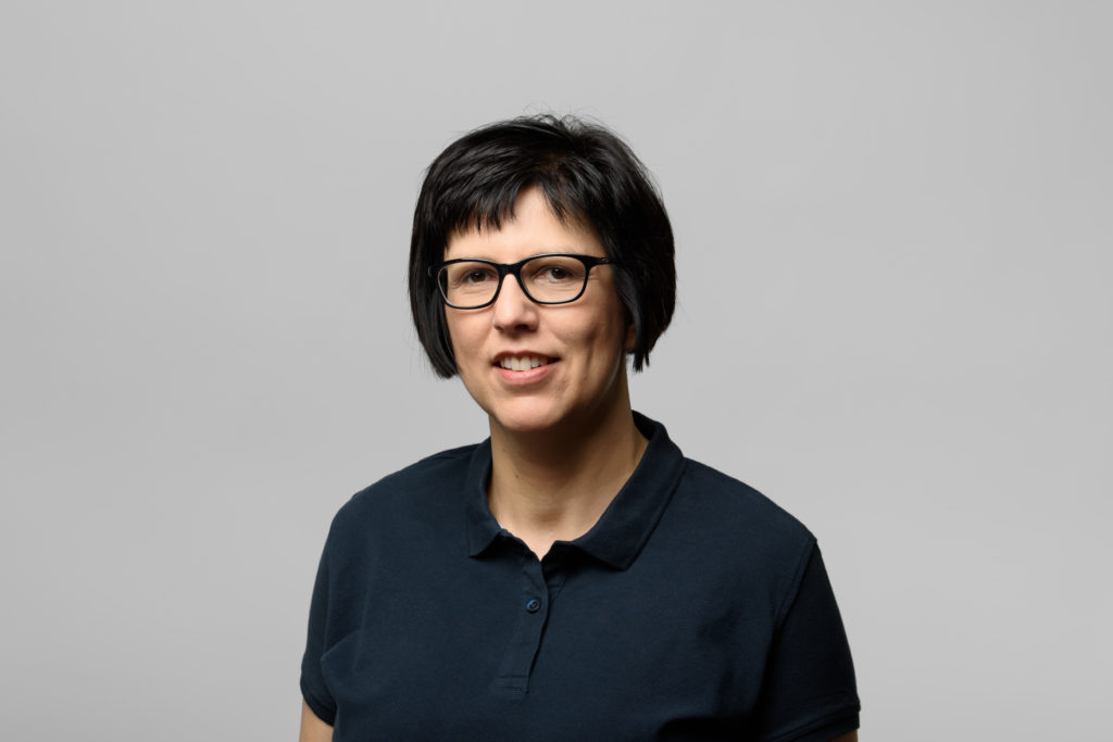 Frau Marquardt mit kurzen, dunklen Haaren und Brille, die in einem neutralen Hintergrund lächelt. In der Trommsdorff Apotheke in Erfurt